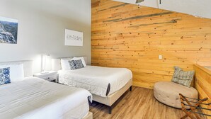 Une chambre avec deux lits, un mur en bois, un ventilateur de plafond et un petit coin salon.