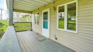 A covered porch with a wooden deck, a door with a blue accent, and a small window with a white frame. - Kayak & Fish: 1 Block to Lakeside Park & Ramp! (Dowagiac)
