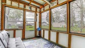 A room with a grey sofa, large windows, and a view of a yard. - Kayak & Fish: 1 Block to Lakeside Park & Ramp! (Dowagiac)