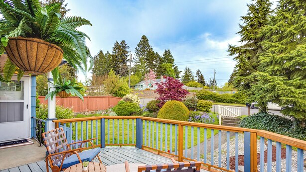 A wooden deck with outdoor furniture, a railing, and a variety of plants and trees in the background. - Vibrant Tacoma Retreat, Near Point Defiance Park! (Tacoma)