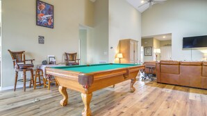 A pool table in a spacious room with wooden flooring, a brown leather sofa, and a television mounted on the wall. - Wilmington Home w/ Sunroom & Private Deck! (Wilmington)