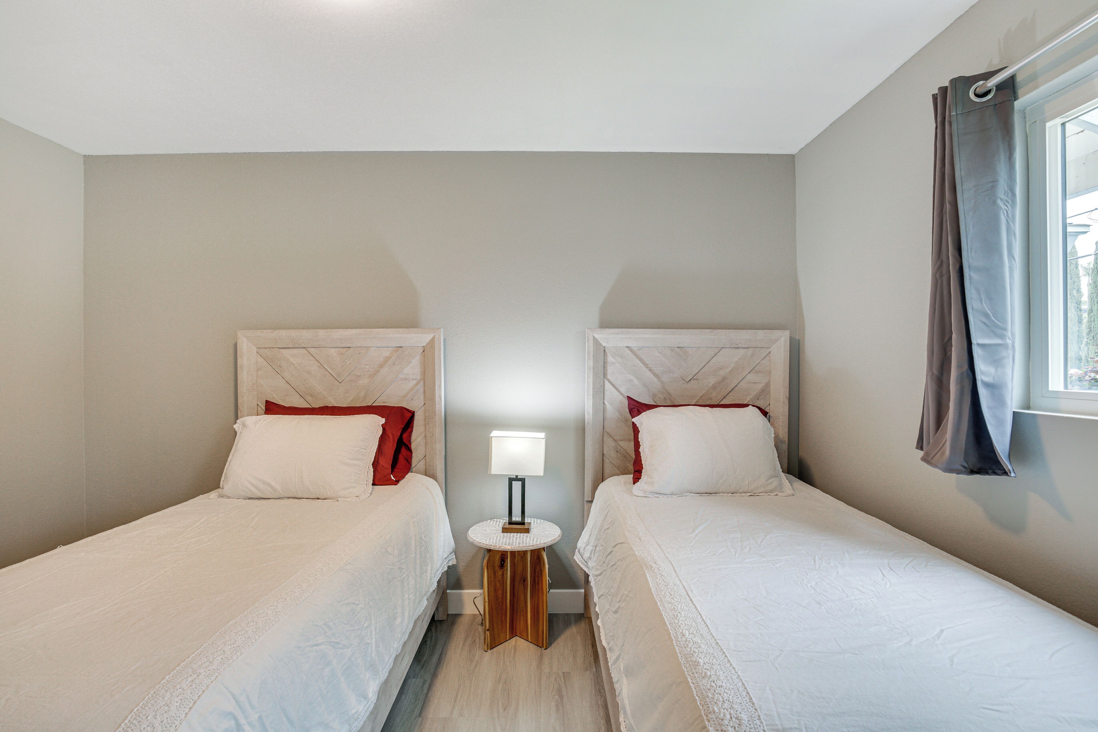 Une chambre d’hôtel avec deux lits simples, une petite table de chevet avec une lampe et une fen être avec des rideaux.