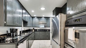 A modern kitchen with stainless steel appliances, dark cabinets, and a tiled floor. - Fireplace, Hot Tub, Patio & Bbq: San Diego Home (Spring Valley)
