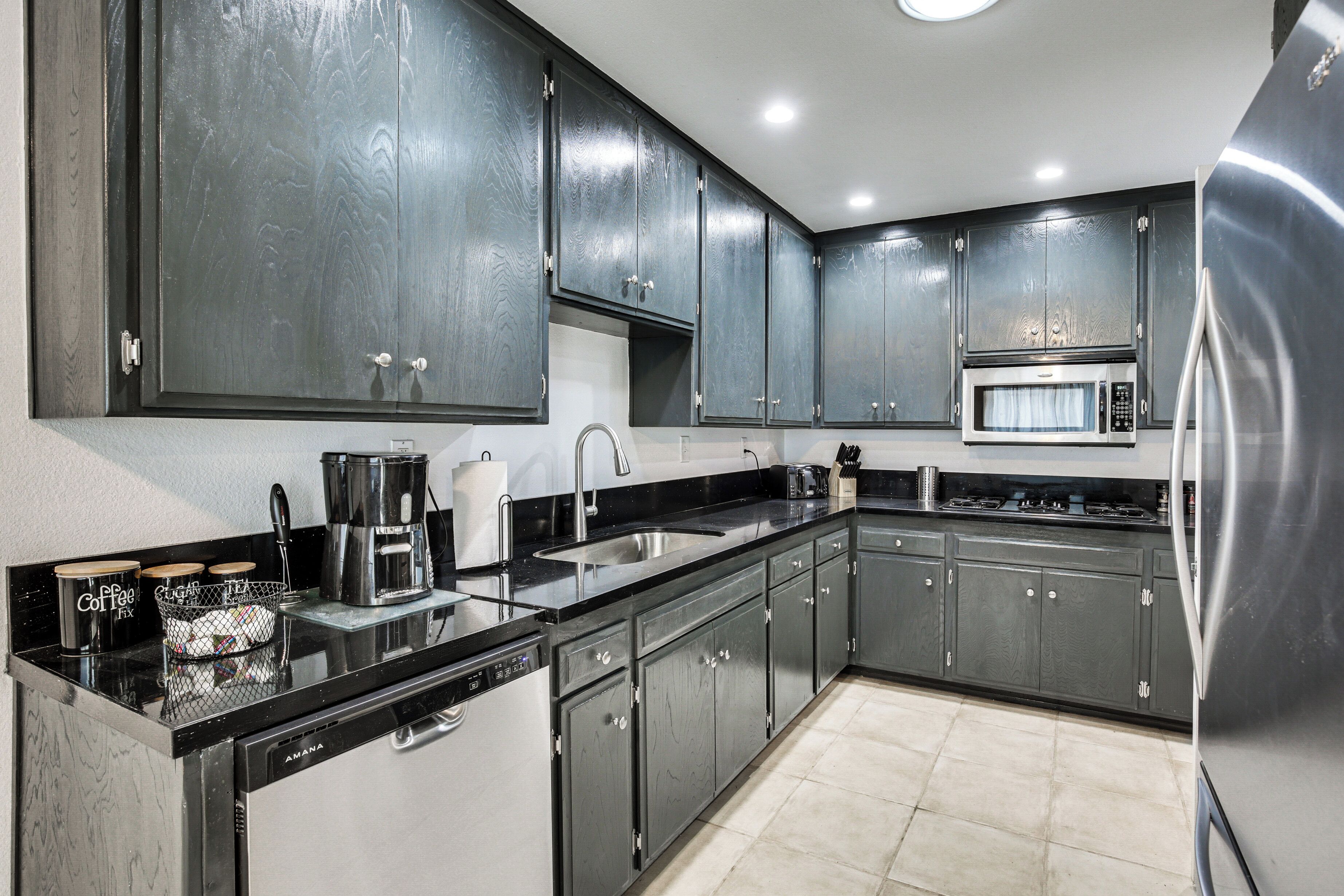 A modern kitchen with dark cabinets, a stainless steel refrigerator, a microwave, and a dishwasher.