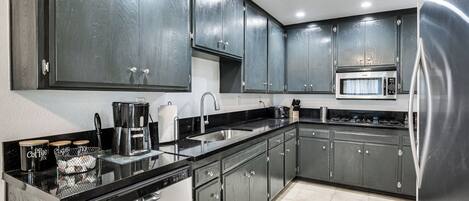 A modern kitchen with dark cabinets, a stainless steel refrigerator, a microwave, and a dishwasher.