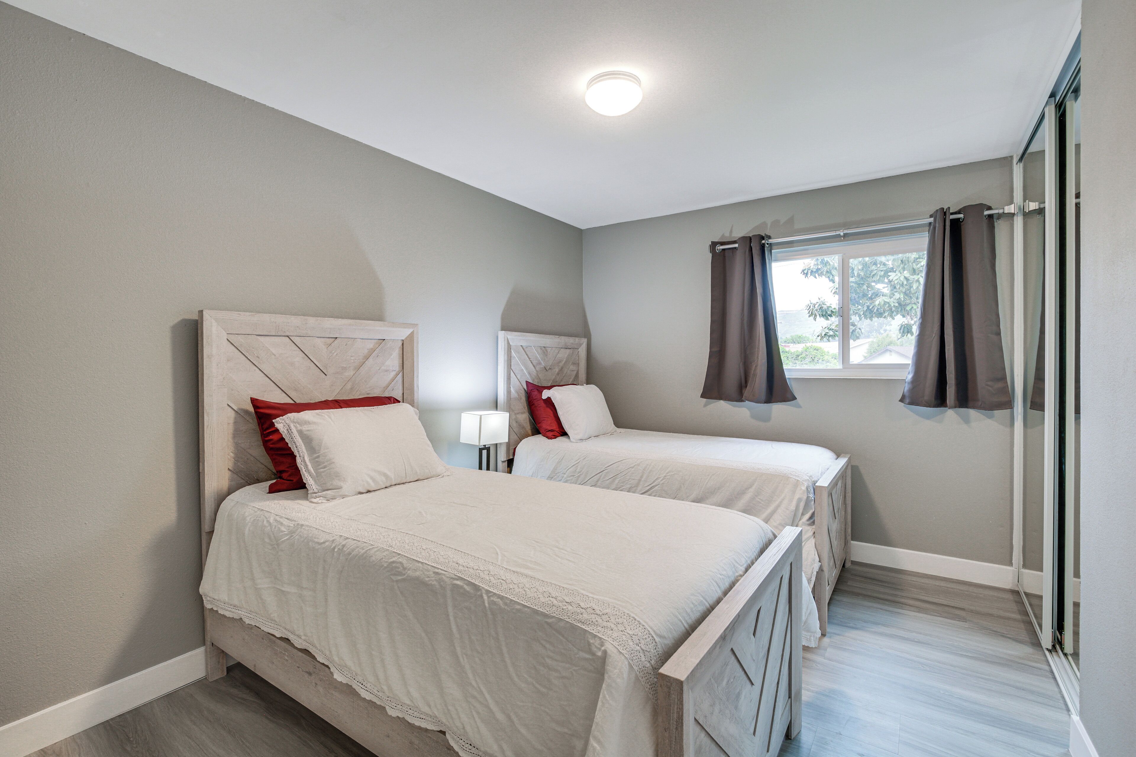 A bedroom with two beds, a window with curtains, and a ceiling light.
