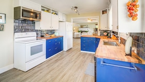 Een moderne keuken met witte apparaten, blauwe kastjes en een houten aanrecht.