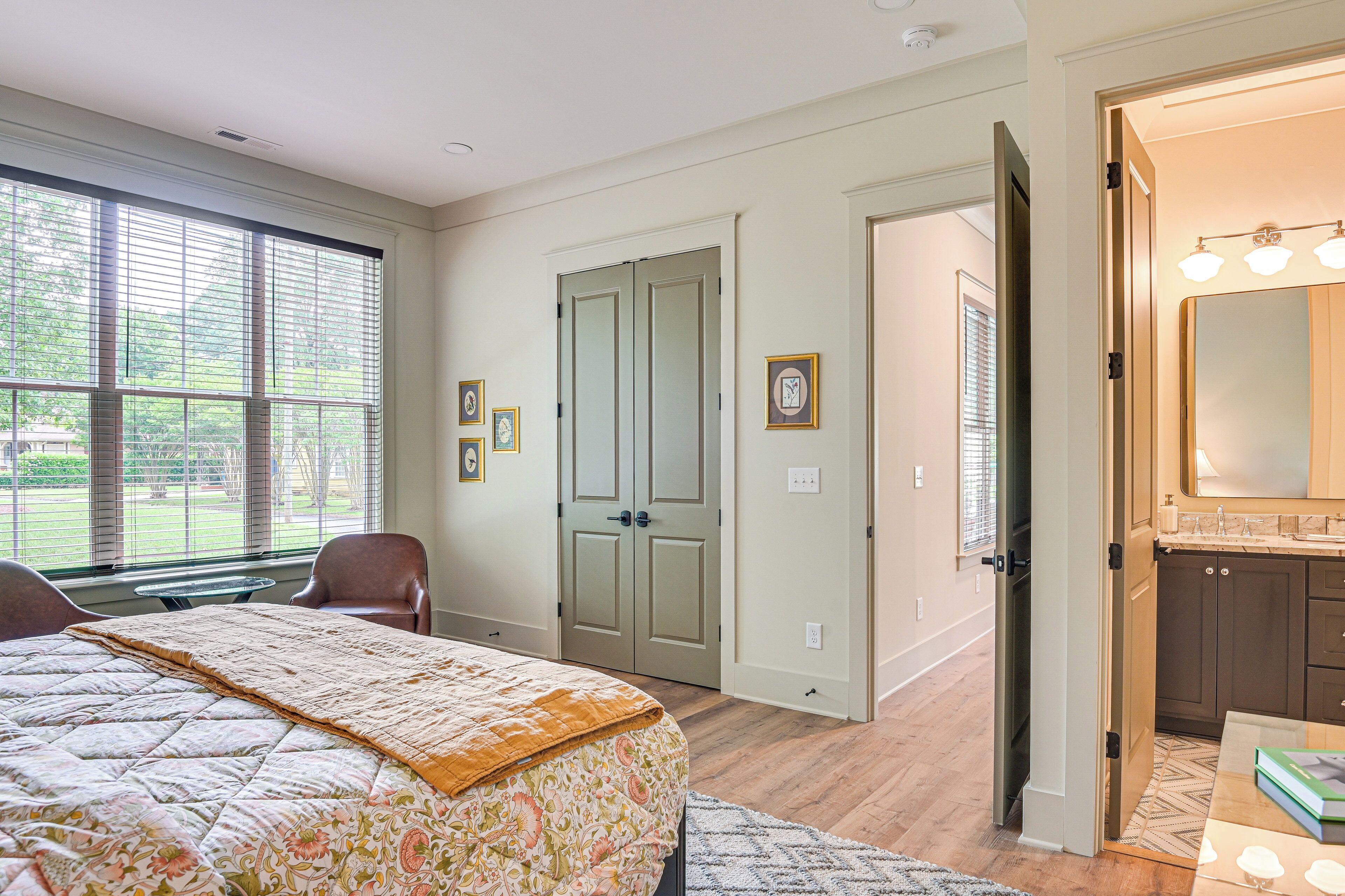 A bedroom with a large bed, a desk, and a bathroom with a mirror and sink.