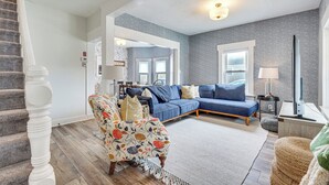 A spacious living room with a blue sectional sofa, a patterned armchair, and a staircase with a white balustrade. - Lovely Ludlow Farmhouse ~ 1 Mi to Town & Slopes! (Ludlow)