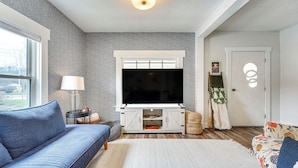 A modern living room with a large flat-screen TV, a blue sofa, a patterned armchair, and a white entertainment unit. - Lovely Ludlow Farmhouse ~ 1 Mi to Town & Slopes! (Ludlow)