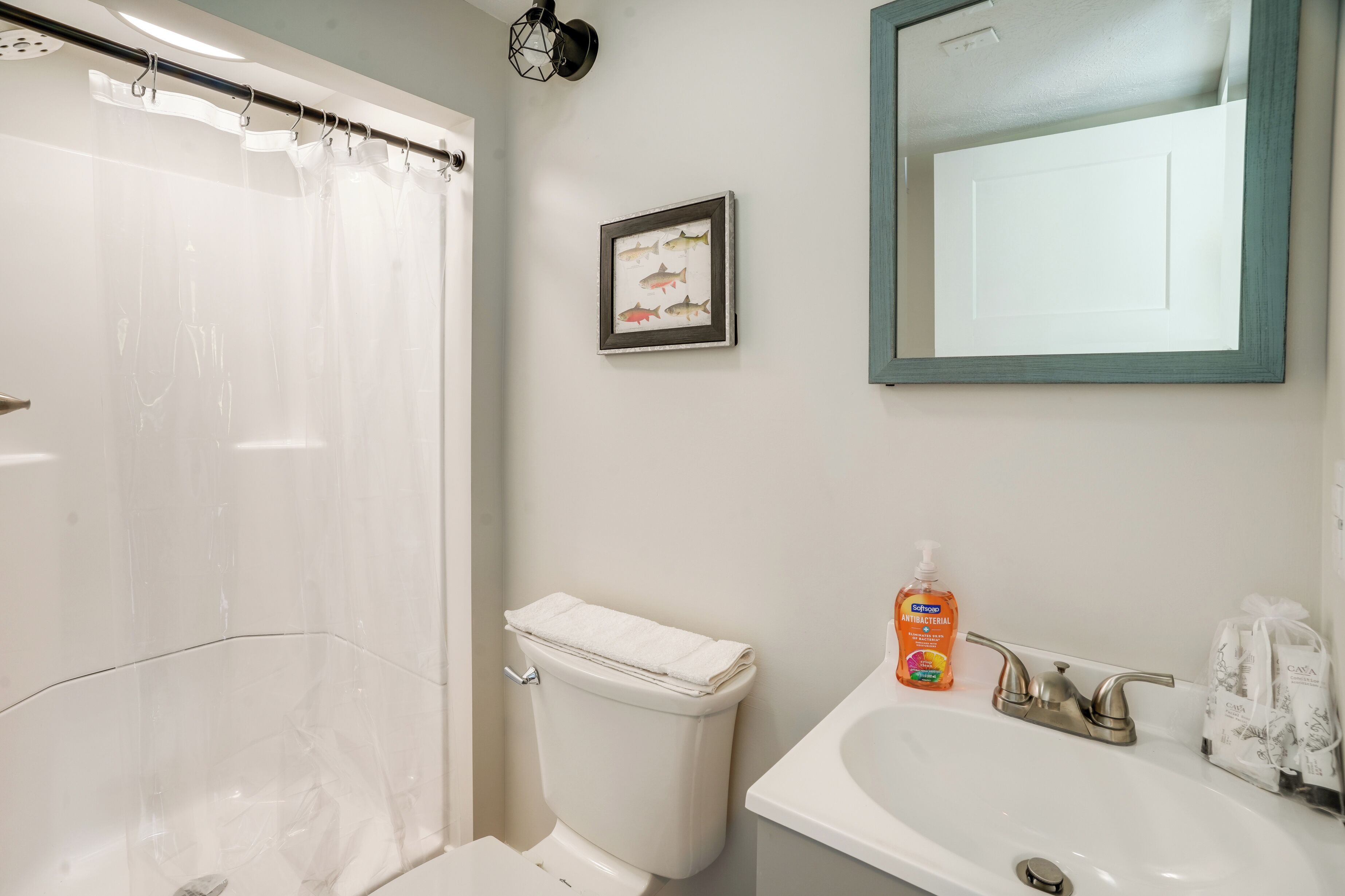 Un baño con ducha, inodoro, lavabo y un cuadro de un pez enmarcado en la pared.
