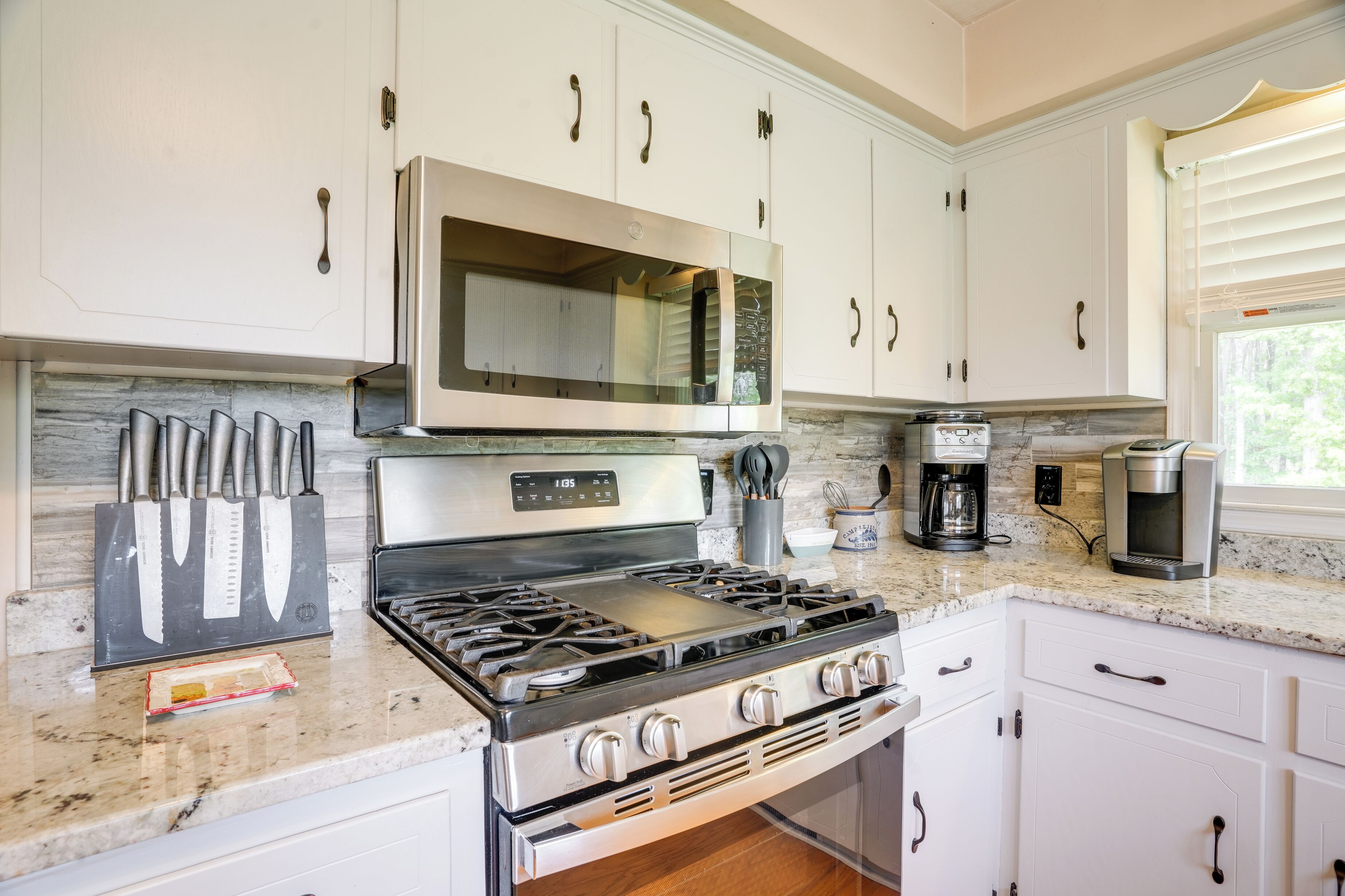 Una cocina con armarios blancos, una estufa de acero inoxidable, un microondas y una cafetera.