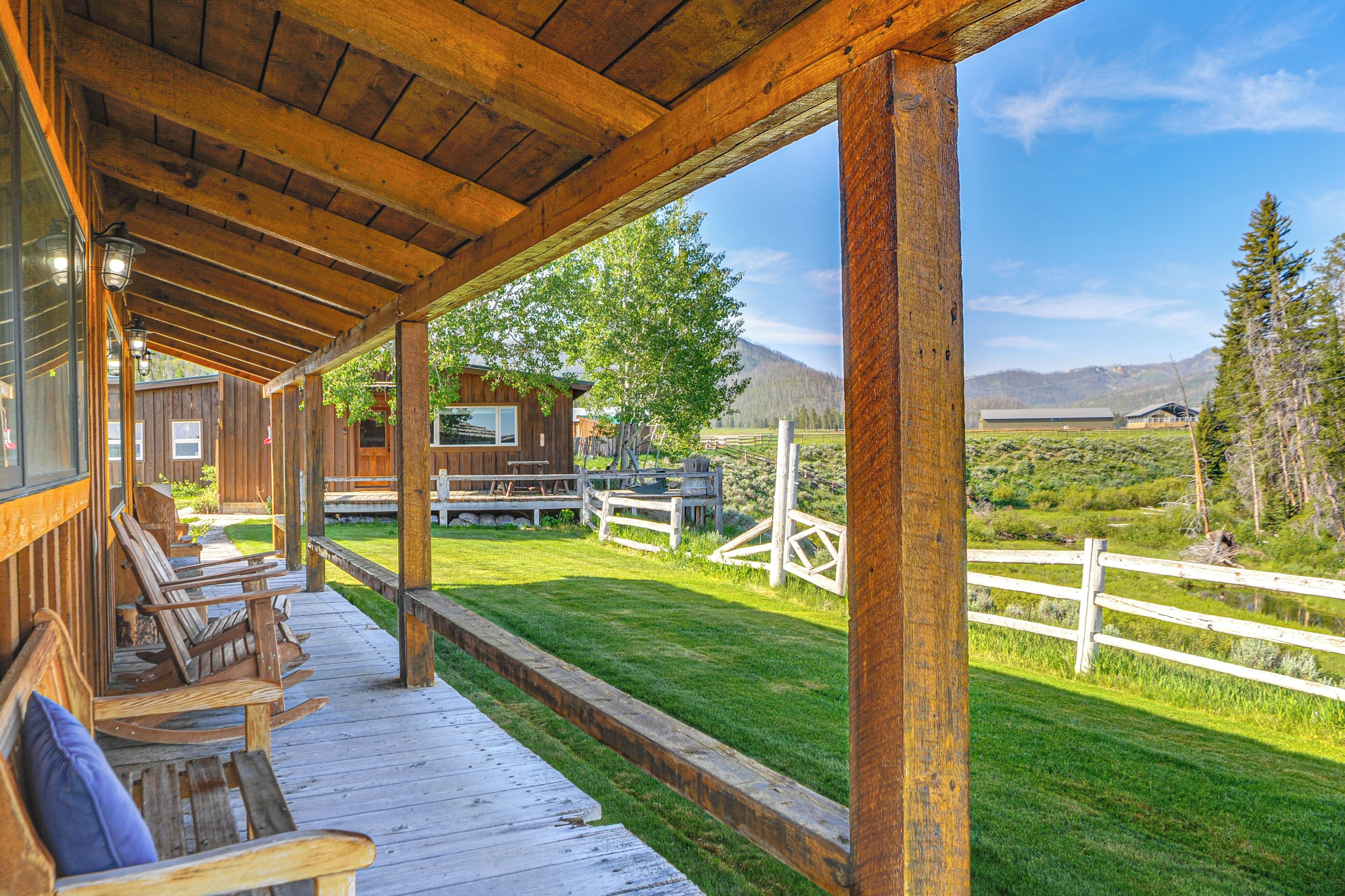A wooden deck with benches, a wooden fence, and a view of a cabin and mountains.