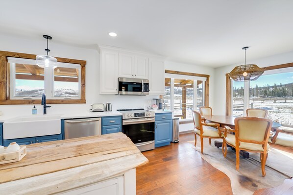 A modern kitchen with white cabinets, a wooden dining table, and a view of a snowy landscape. - Rustic Bondurant Cabin: Fish, Hike, & Bike! (Bondurant)