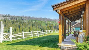 A wooden cabin with a porch, surrounded by a white fence and a forested hillside.