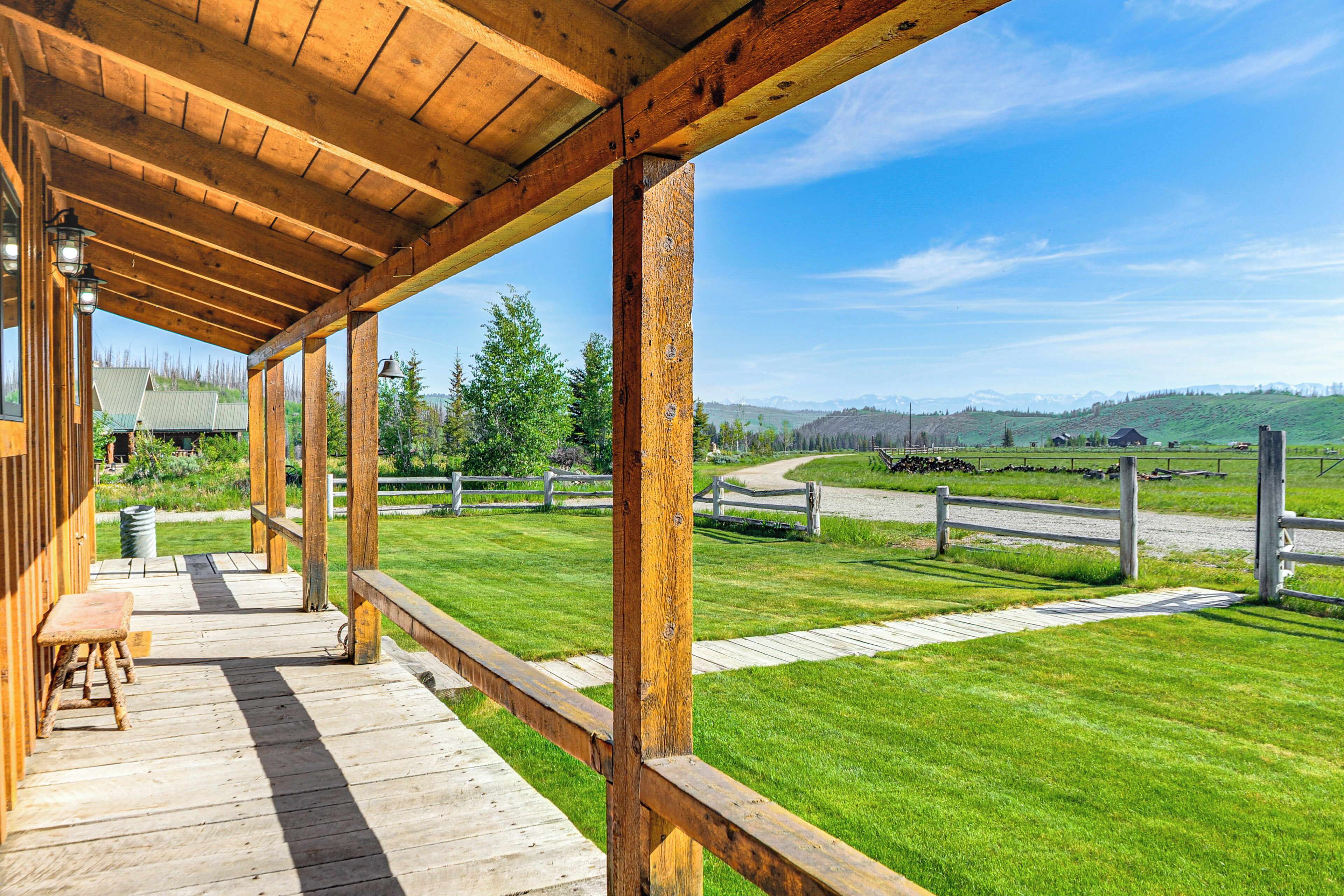 A wooden deck with a bench, overlooking a grassy area with a fence and a clear sky.