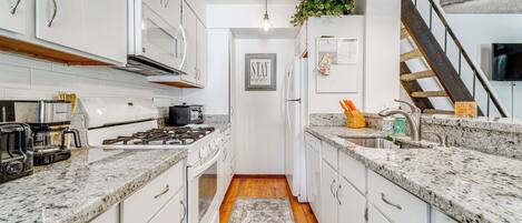 A modern kitchen with white cabinets, granite countertops, a stainless steel range hood, and a wooden floor.