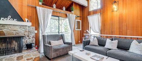 A cozy living room with a stone fireplace, two sofas, a coffee table, and a view of the outdoors.