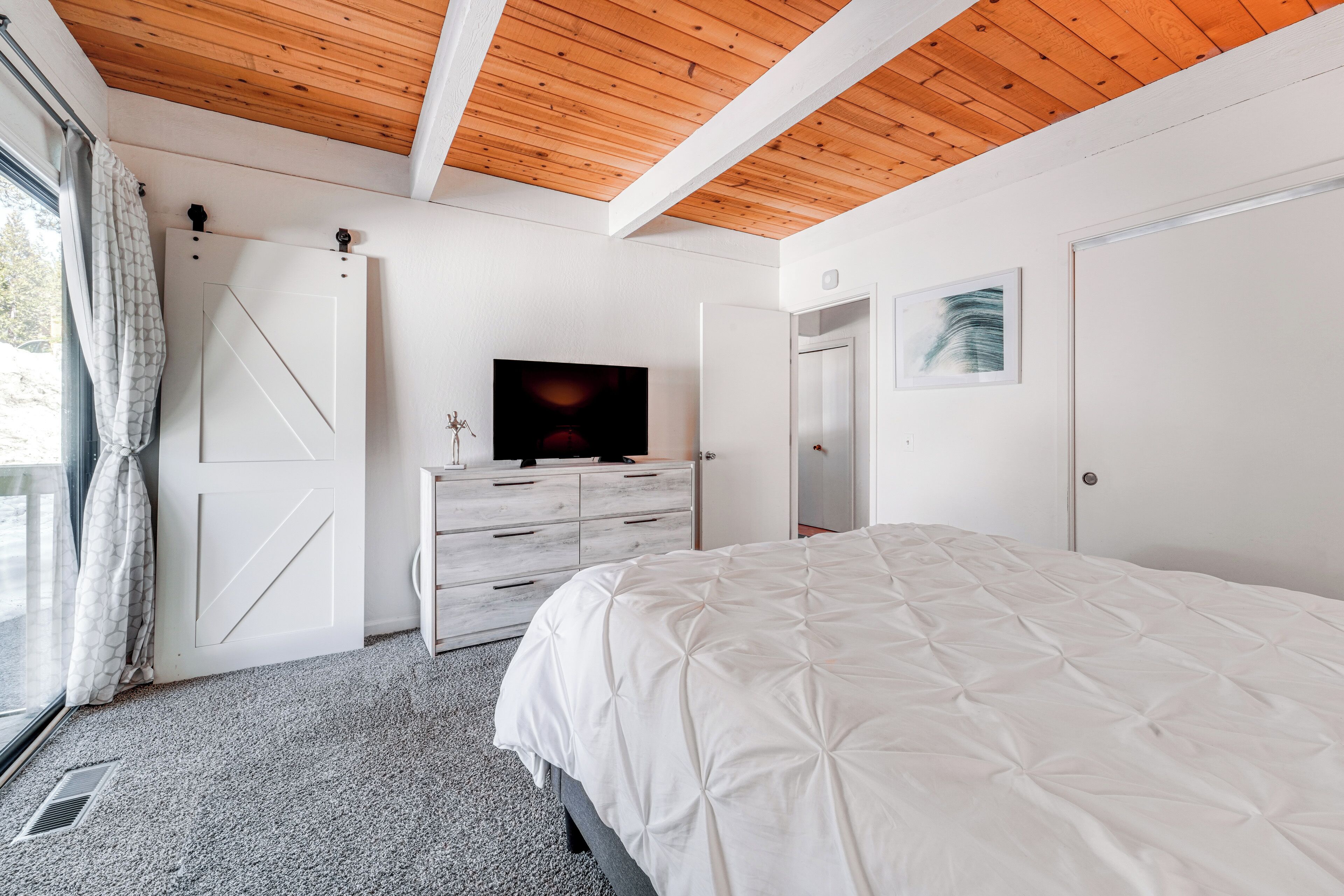 A bedroom with a large bed, a TV on a dresser, and a wooden ceiling.
