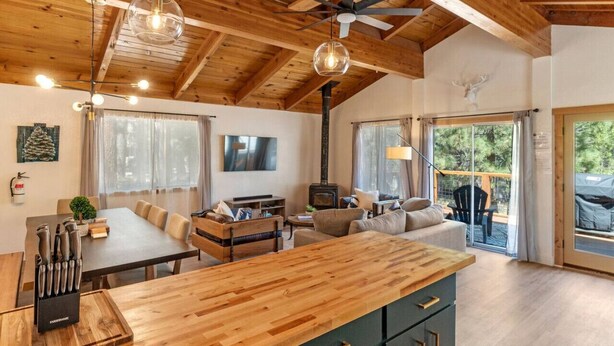 A cozy cabin interior with a wooden ceiling, a dining area, a sofa, and a fireplace.