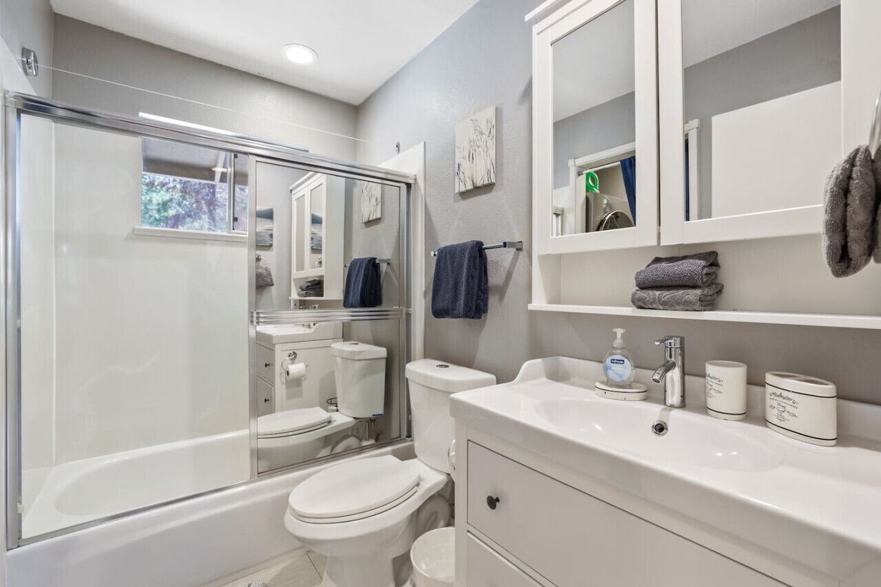 Un baño moderno con ducha de vidrio, un lavamanos blanco con dispensador de jabón y un inodoro.