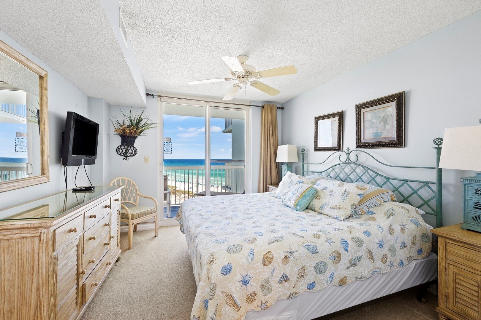 A bedroom with a bed, a dresser, a television, and a view of the beach.