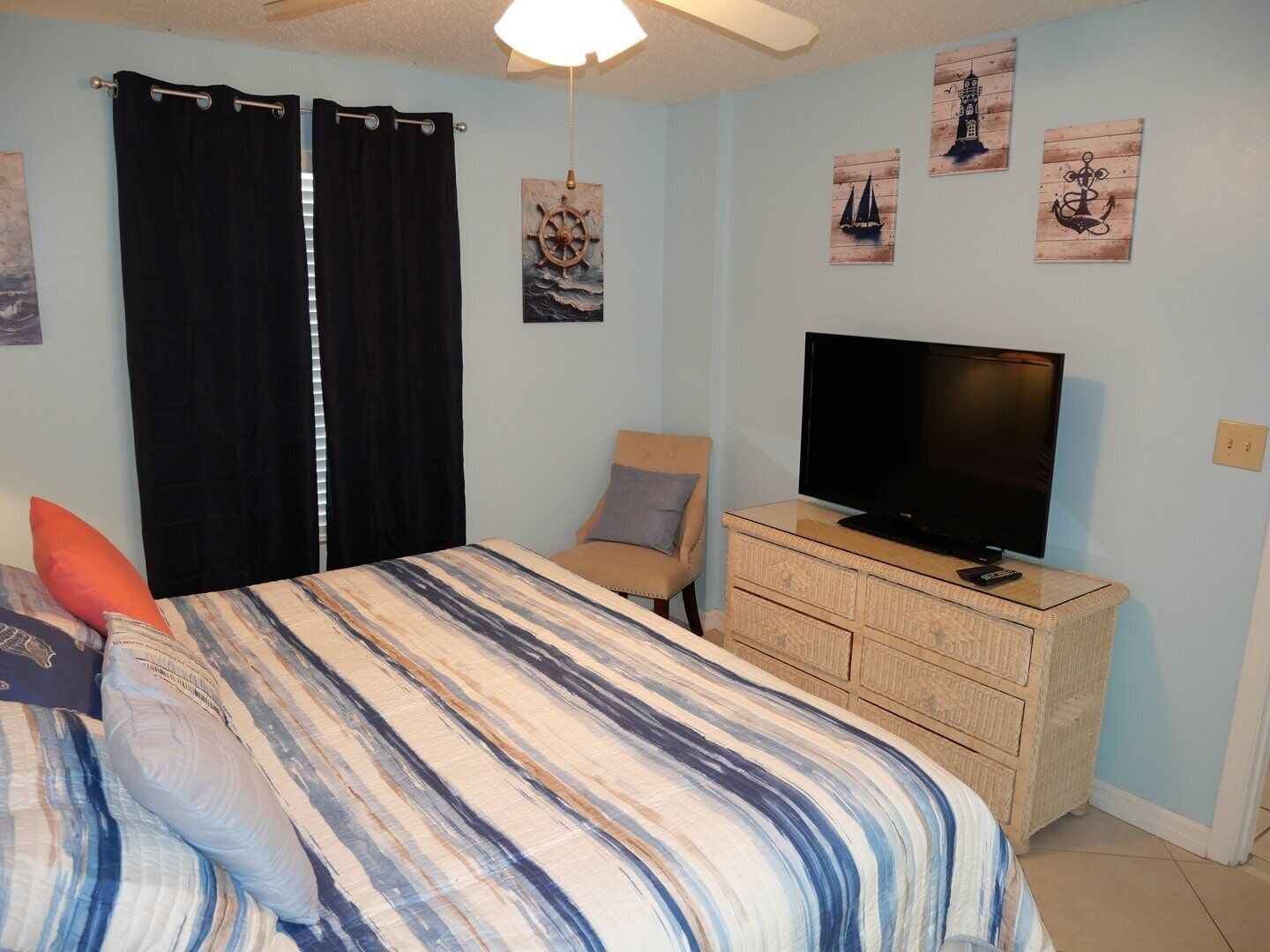 A bedroom with a bed, a television on a dresser, and nautical-themed wall art.