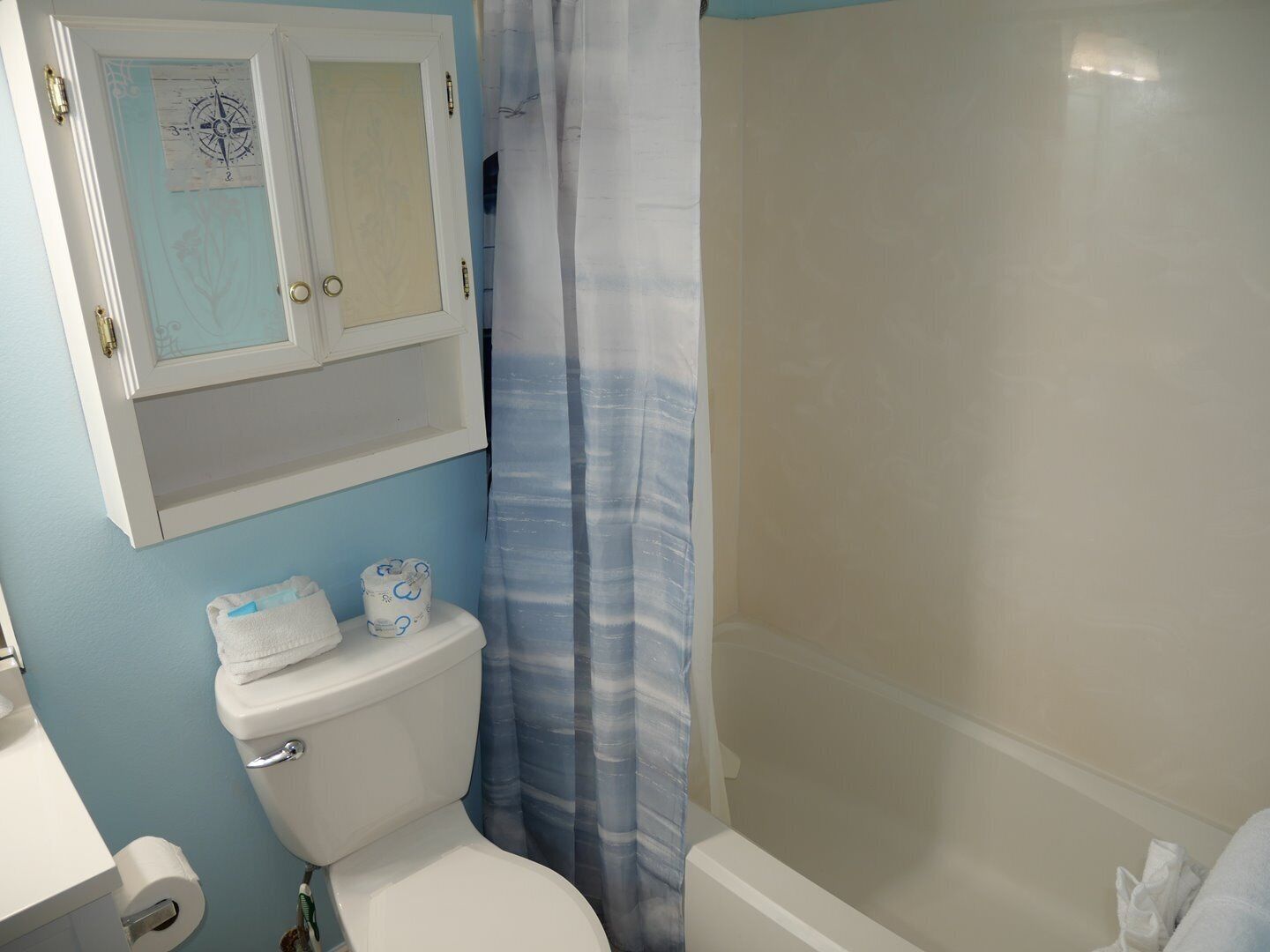 A bathroom with a toilet, a sink, a shower with a curtain, and a cabinet with a compass design.