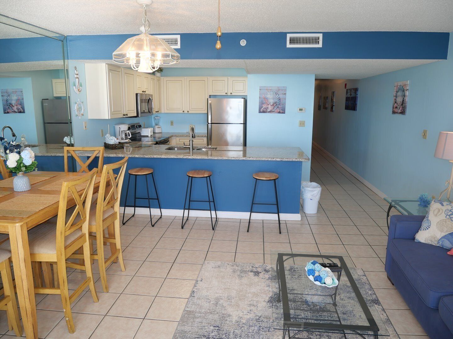 A modern kitchen with a central island, bar stools, a dining table with chairs, a blue sofa, and a coffee table.