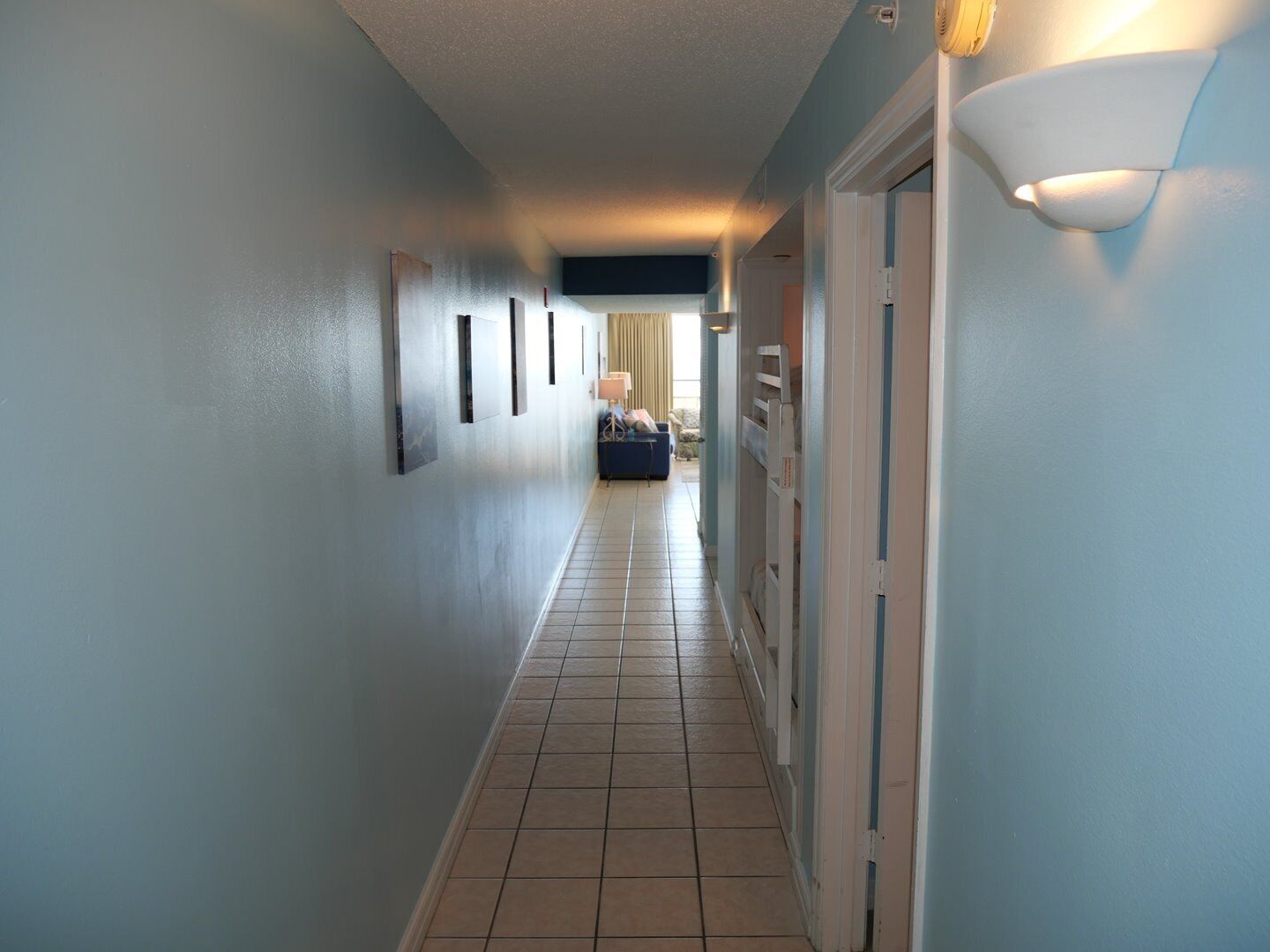 A hotel hallway with a tiled floor, light blue walls, and a door on the right.