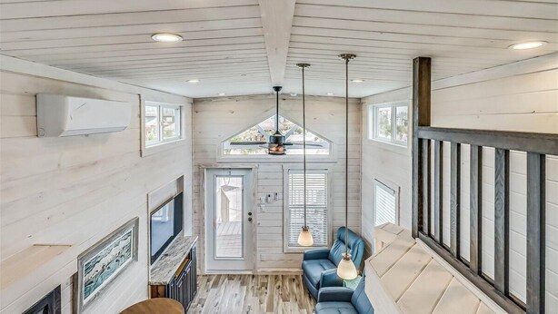 A spacious loft with a high ceiling, exposed wooden beams, a built-in fireplace, and a cozy seating area with a blue sofa and pendant lights. - Margarita Time Sfth1 1 Bedroom Home by RedAwning (Port Aransas)