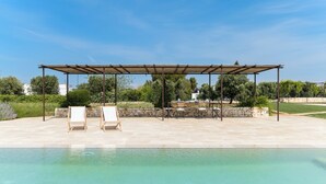 A pool area with a pergola, lounge chairs, and a stone wall. - Casa Blue con piscina by Wonderful Italy (Ostuni)