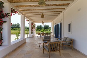 Portico esterno coperto con tavolo e sedie, una lampada a sospensione e vista su piante.