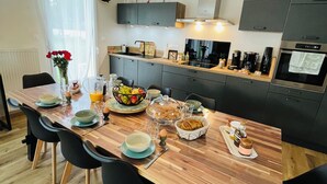 Een moderne keuken met een houten eettafel, zwarte stoelen en diverse ontbijtartikelen.