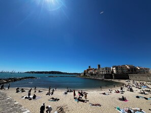 A beach with people sunbathing and swimming, a clear blue sky, and buildings in the background. - Antibes - Appartement 2 Pièces - 4 Personnes - Climatisation - Proche Centre (Antibes)