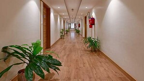 A hotel hallway with wooden flooring, potted plants, and fire extinguishers on the walls. - Hotel Page One (Ahmedabad)