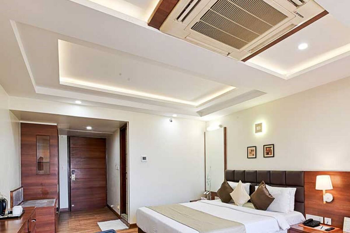 A modern hotel room with a large bed, a desk, a chair, and a bedside table.