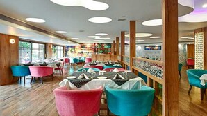 A restaurant with wooden floors, colorful chairs, and a modern ceiling design. - Hotel Page One (Ahmedabad)