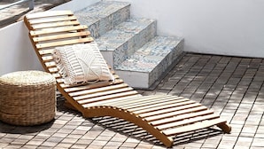 A patio with wooden loungers, a woven ottoman, and a patterned stone staircase.