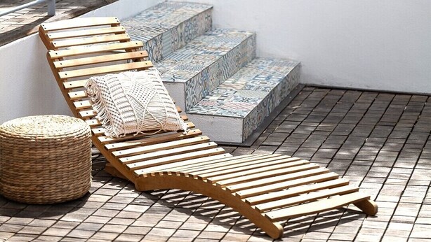 Un patio con sillones de madera, un otoman tejido y una escalera de piedra con diseño.