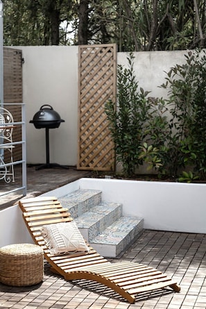A patio with wooden loungers, a woven ottoman, and a patterned stone staircase.