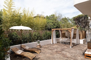 A patio with wooden lounge chairs, a pergola with white curtains, and a table with chairs.