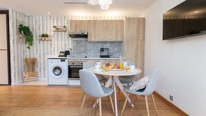 A modern kitchen with wooden cabinets, a washing machine, and a dining area with a round table and chairs.