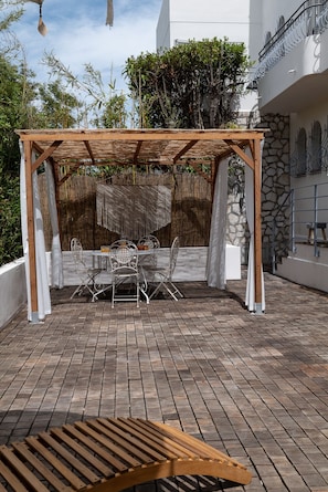 An outdoor patio with a wooden pergola, a round table with chairs, and a bench.