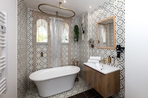 A bathroom with a freestanding bathtub, a wooden vanity with a mirror, and patterned wallpaper.
