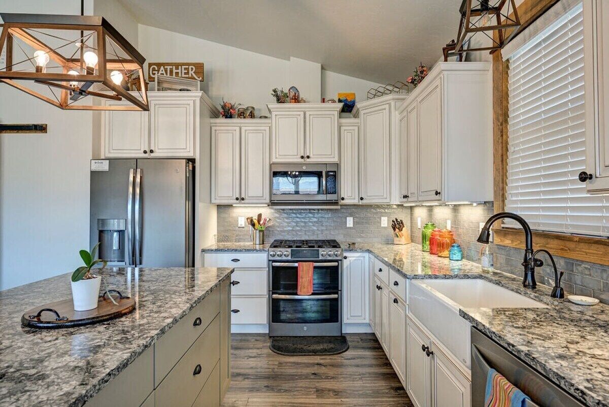 A modern kitchen with white cabinets, a granite countertop, a built-in oven, and a stainless steel refrigerator.
