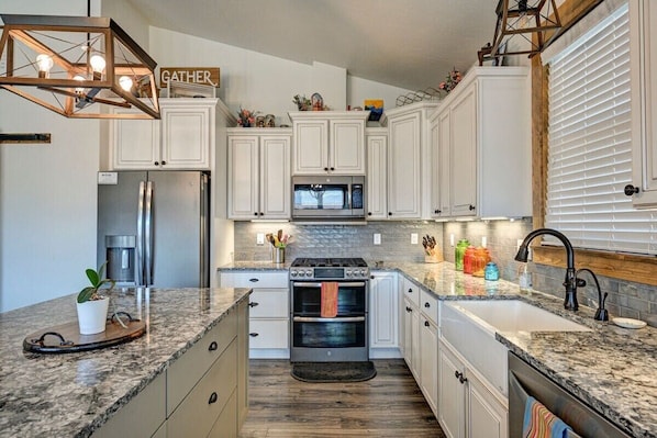 A modern kitchen with white cabinets, a granite countertop, a built-in oven, and a stainless steel refrigerator.