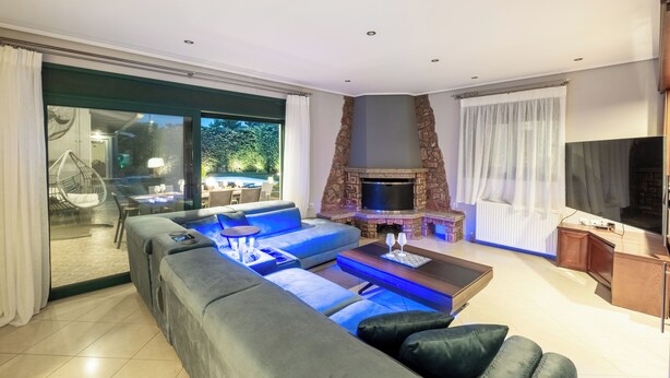 A modern living room with a stone fireplace, a large sofa, and a dining area with outdoor seating.