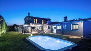 A two-story house with a swimming pool, outdoor seating, and a well-lit patio area.
