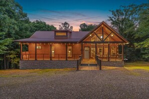 A log cabin with a stone foundation, large windows, and a porch with string lights.